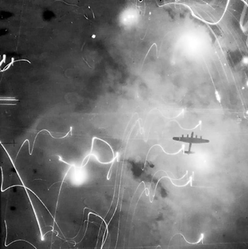 Avro Lancaster of No. 1 Group, Bomber Command, silhouetted against flares, smoke and explosions during the attack on Hamburg, Germany (1943) - Public Domain