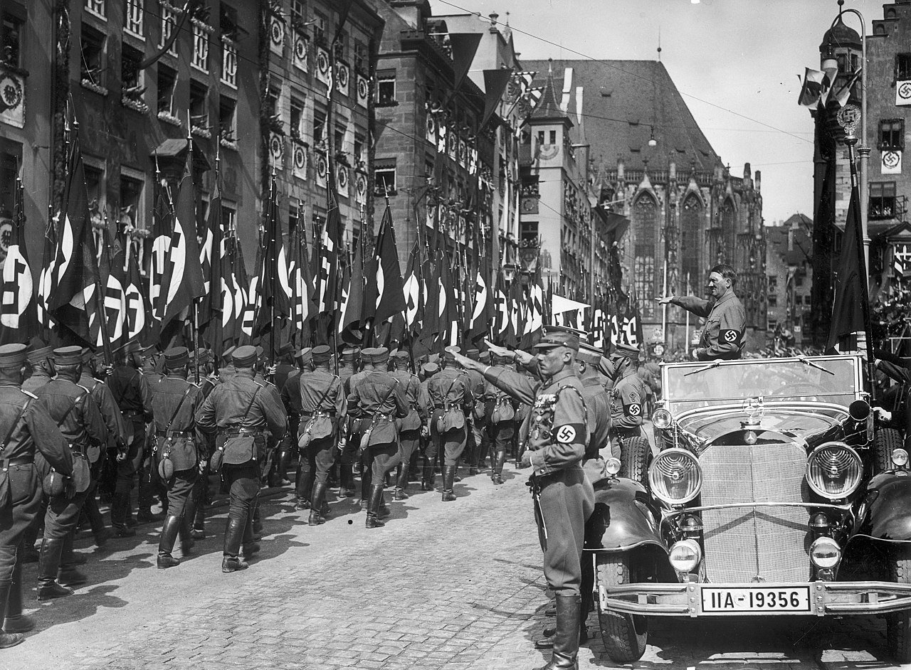 The Nazi Party Rally in Nuremberg , September 10th–16th 1935; Adolf Hitler salutes in front of the Blood Flag - Public Domain
